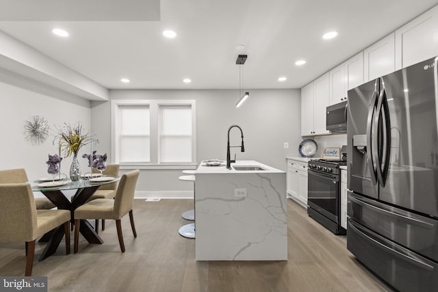 kitchen with decorative light fixtures, white cabinets, black gas stove, a sink, and stainless steel fridge