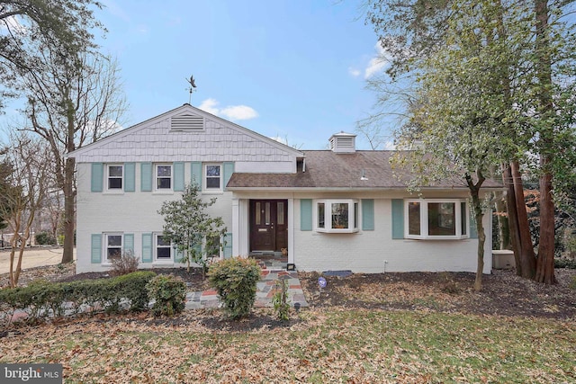 split level home featuring brick siding, a chimney, a front lawn, and roof with shingles