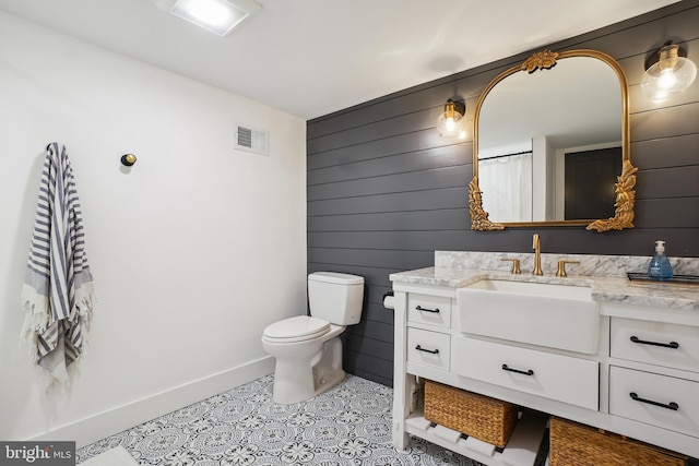 full bathroom featuring wooden walls, visible vents, toilet, tile patterned floors, and vanity