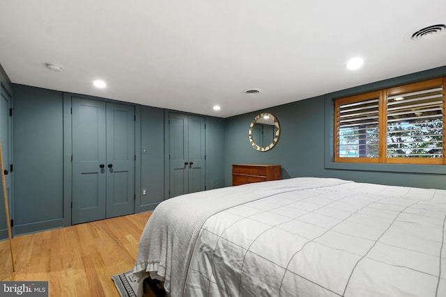 bedroom with light wood-type flooring, two closets, visible vents, and recessed lighting