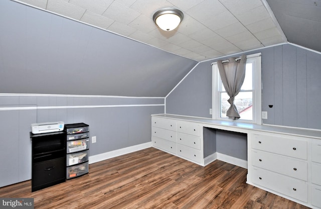 unfurnished office with vaulted ceiling, built in desk, and dark hardwood / wood-style floors