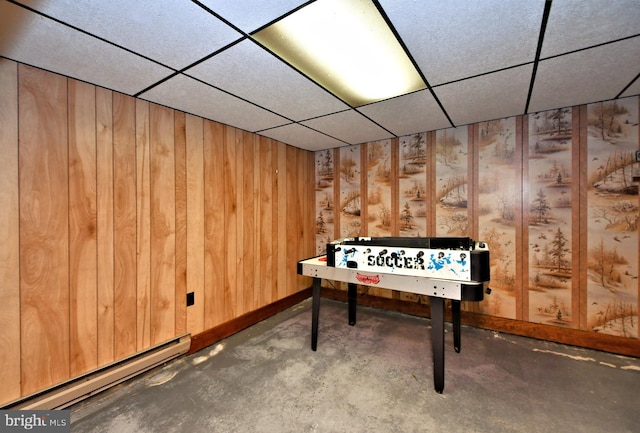 game room with concrete flooring, a drop ceiling, wood walls, and a baseboard radiator