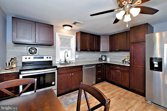 kitchen with appliances with stainless steel finishes, sink, light hardwood / wood-style flooring, light stone counters, and decorative backsplash