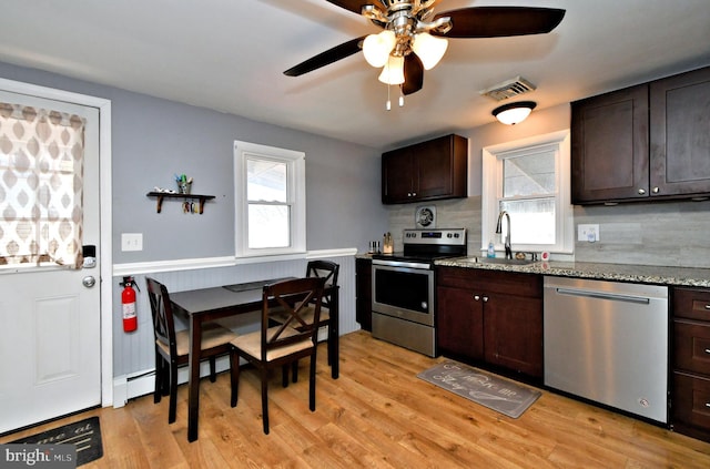 kitchen with appliances with stainless steel finishes, light hardwood / wood-style flooring, dark brown cabinets, light stone counters, and sink