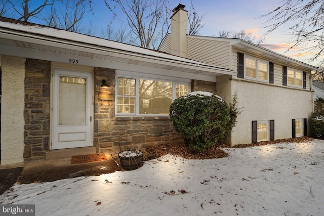 doorway to property with stone siding, a chimney, and stucco siding