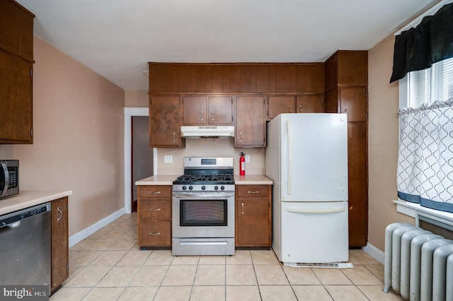 kitchen with radiator heating unit, appliances with stainless steel finishes, and light tile patterned flooring