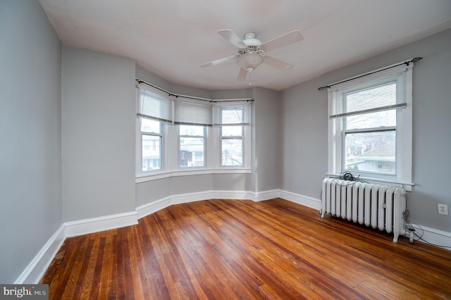 spare room featuring ceiling fan, radiator, a healthy amount of sunlight, and wood-type flooring