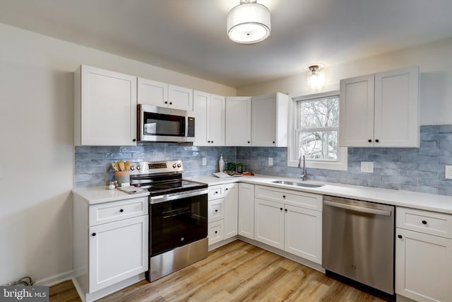 kitchen with appliances with stainless steel finishes, white cabinets, light countertops, and a sink