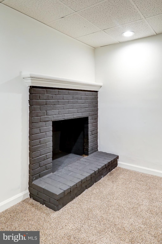 interior details with a brick fireplace, baseboards, a drop ceiling, and carpet flooring