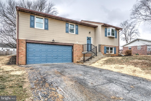 split foyer home featuring brick siding, an attached garage, and aphalt driveway