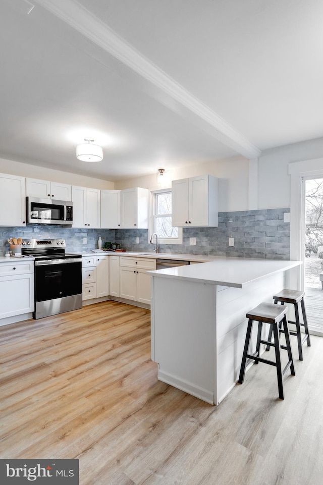 kitchen featuring a breakfast bar area, stainless steel appliances, tasteful backsplash, light countertops, and white cabinetry