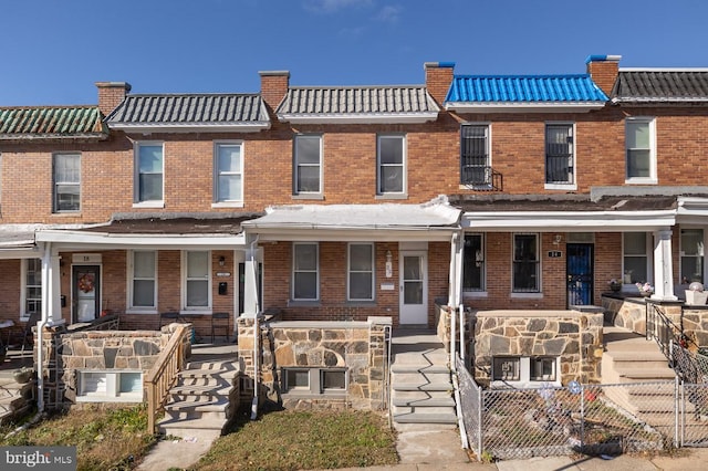 multi unit property with covered porch, a tile roof, fence, and brick siding