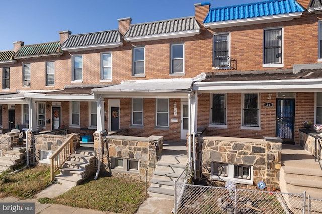 townhome / multi-family property with covered porch, a fenced front yard, a tile roof, and brick siding