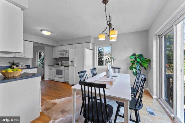 dining area with a chandelier, baseboards, visible vents, and light wood finished floors