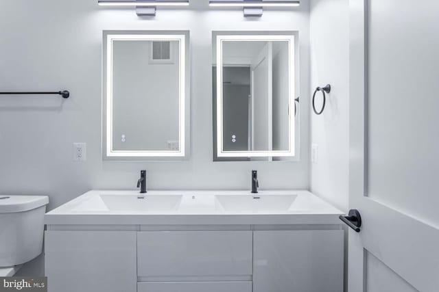 bathroom with visible vents, double vanity, a sink, and toilet