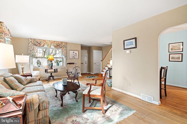 living room featuring light wood-style flooring, visible vents, baseboards, arched walkways, and stairs