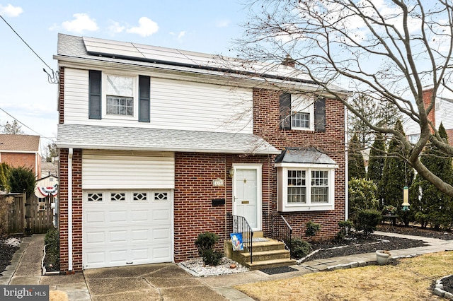 view of front facade featuring roof mounted solar panels, a shingled roof, an attached garage, and brick siding