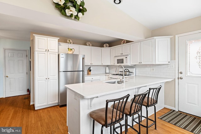 kitchen with light countertops, a kitchen bar, a peninsula, white appliances, and white cabinetry