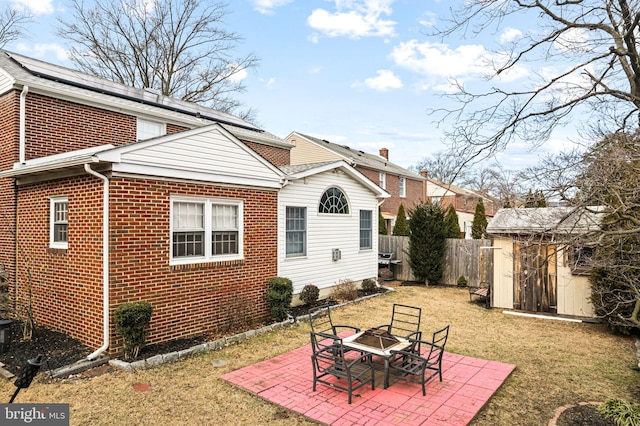 rear view of property with fence, brick siding, an outdoor structure, a patio area, and a shed