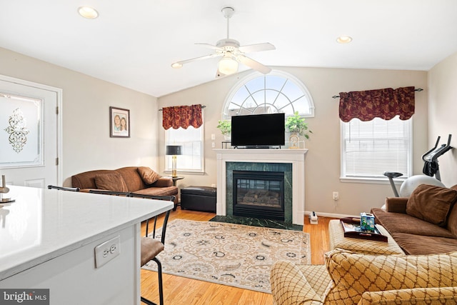 living room featuring ceiling fan, light wood-style floors, lofted ceiling, and a high end fireplace