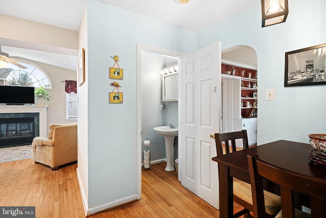 dining space with arched walkways, baseboards, light wood finished floors, and a glass covered fireplace