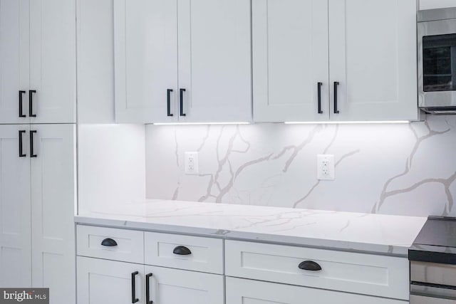 details featuring light stone countertops, white cabinetry, and stainless steel microwave