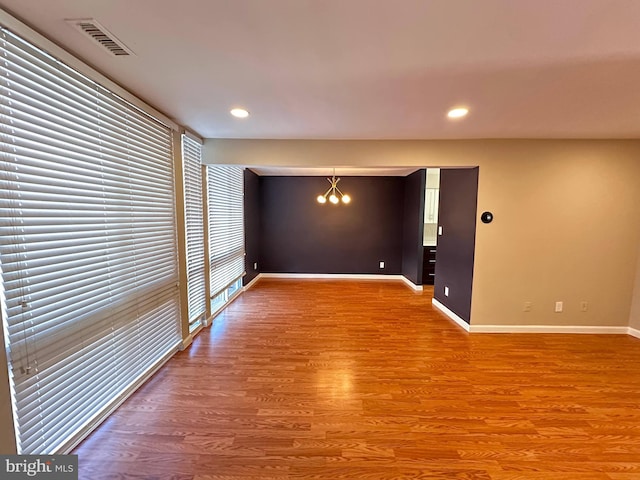 spare room with hardwood / wood-style floors and an inviting chandelier