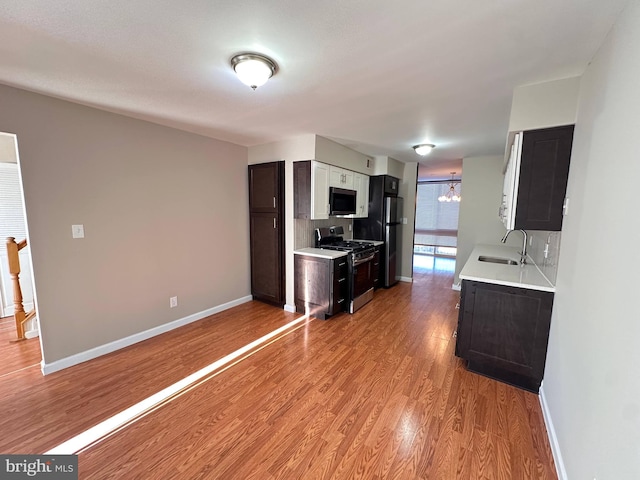 kitchen featuring appliances with stainless steel finishes, light hardwood / wood-style flooring, decorative backsplash, sink, and an inviting chandelier