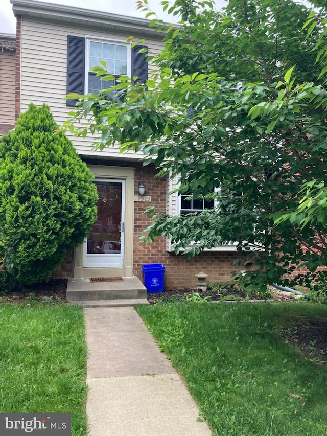 doorway to property with brick siding and a lawn