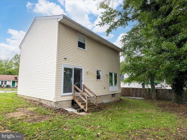 rear view of property with entry steps, fence, and a lawn