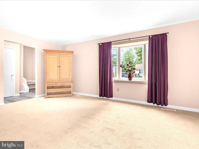 carpeted empty room featuring visible vents, stairway, and baseboards