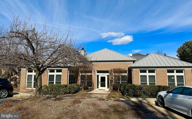 view of front facade with a standing seam roof, brick siding, metal roof, and a chimney