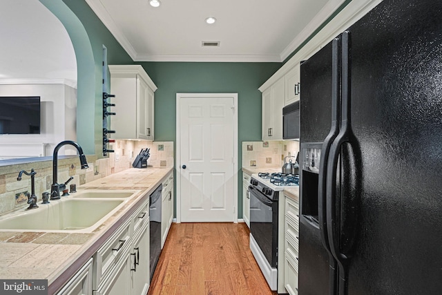 kitchen featuring a sink, visible vents, light wood-style floors, ornamental molding, and black appliances