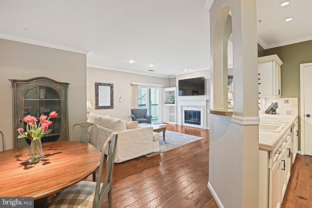 dining room with dark wood-style floors, arched walkways, crown molding, and a fireplace