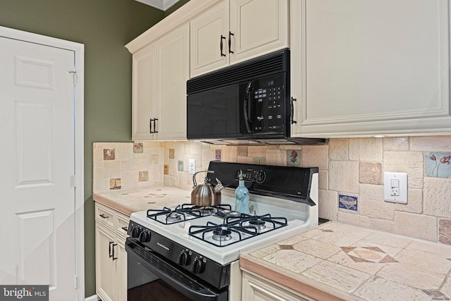 kitchen featuring range with gas cooktop, tile countertops, decorative backsplash, white cabinets, and black microwave