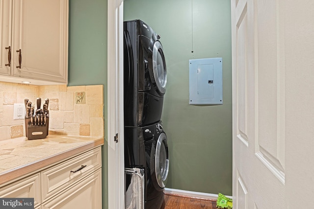 clothes washing area featuring dark wood-type flooring, stacked washer and clothes dryer, electric panel, and baseboards