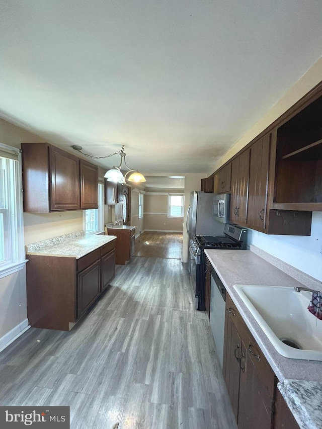 kitchen featuring decorative light fixtures, light countertops, appliances with stainless steel finishes, a sink, and dark brown cabinets