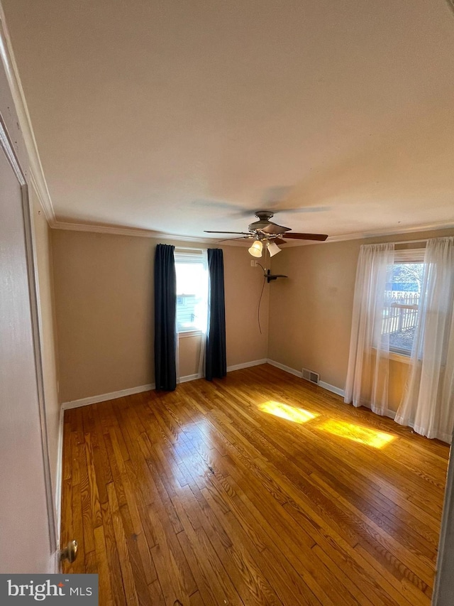 spare room featuring visible vents, crown molding, baseboards, and wood finished floors