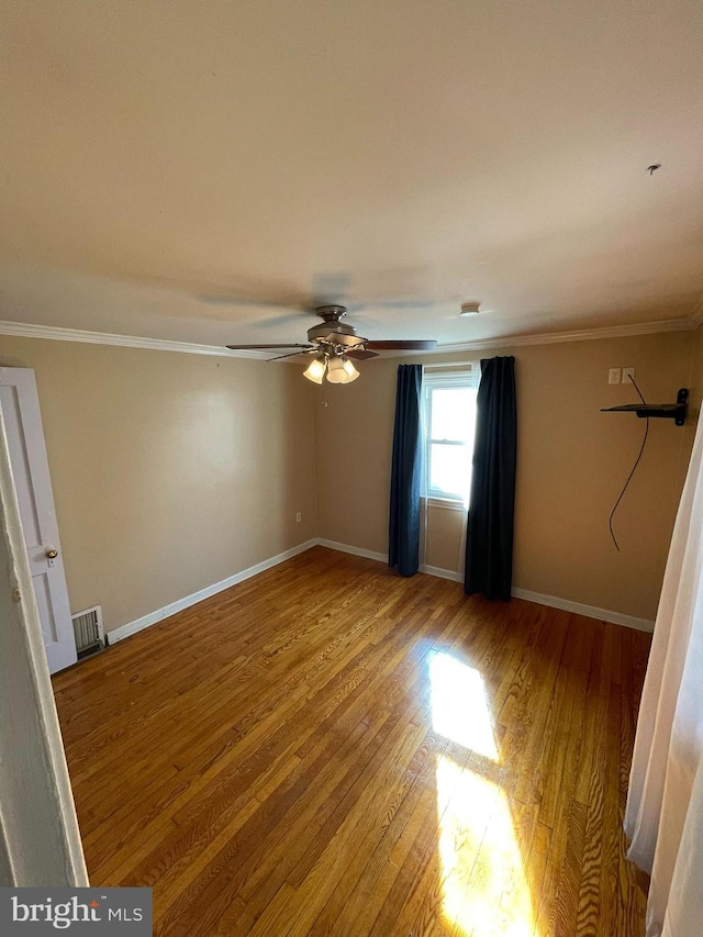 empty room with baseboards, wood finished floors, visible vents, and crown molding