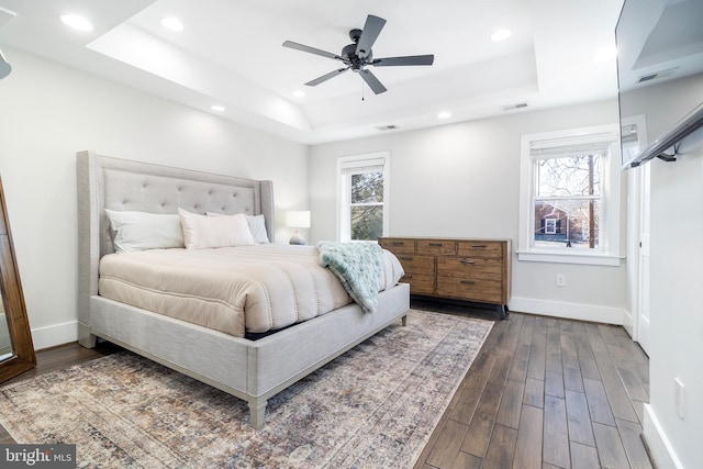 bedroom featuring dark wood finished floors, visible vents, multiple windows, and a tray ceiling