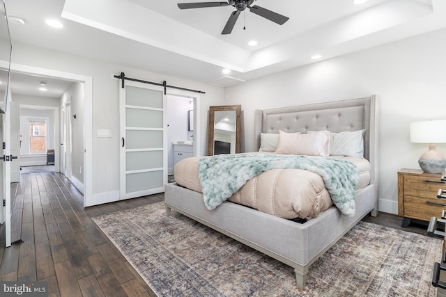 bedroom featuring dark wood-type flooring, recessed lighting, a barn door, baseboards, and a raised ceiling