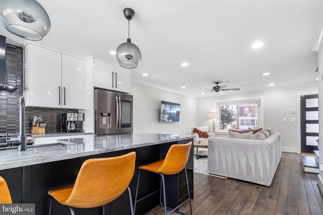 kitchen featuring a breakfast bar area, stainless steel refrigerator with ice dispenser, backsplash, and ornamental molding