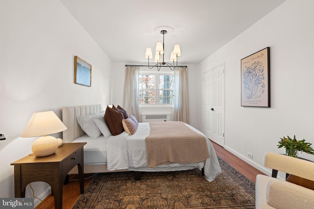 bedroom featuring an inviting chandelier, dark wood-type flooring, and a wall unit AC