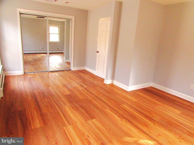 unfurnished bedroom featuring a baseboard radiator, a closet, and light wood-type flooring