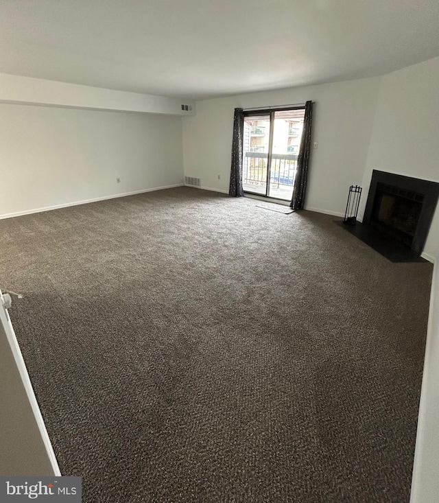 unfurnished living room with dark carpet, a fireplace with flush hearth, visible vents, and baseboards