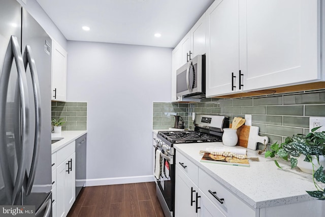 kitchen featuring appliances with stainless steel finishes, light stone counters, dark hardwood / wood-style flooring, white cabinets, and decorative backsplash