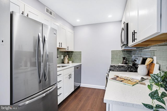 kitchen with dark wood-type flooring, stainless steel appliances, light stone countertops, backsplash, and white cabinetry