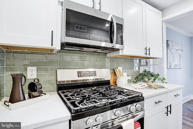 kitchen featuring white cabinetry, light stone counters, appliances with stainless steel finishes, crown molding, and decorative backsplash