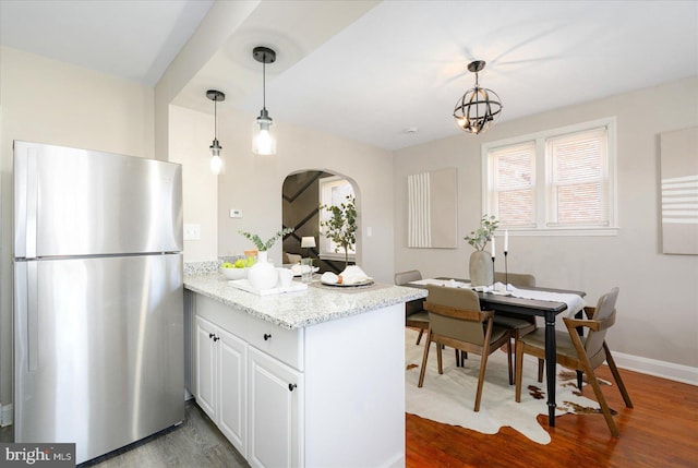 kitchen with hanging light fixtures, light stone countertops, white cabinets, stainless steel fridge, and kitchen peninsula