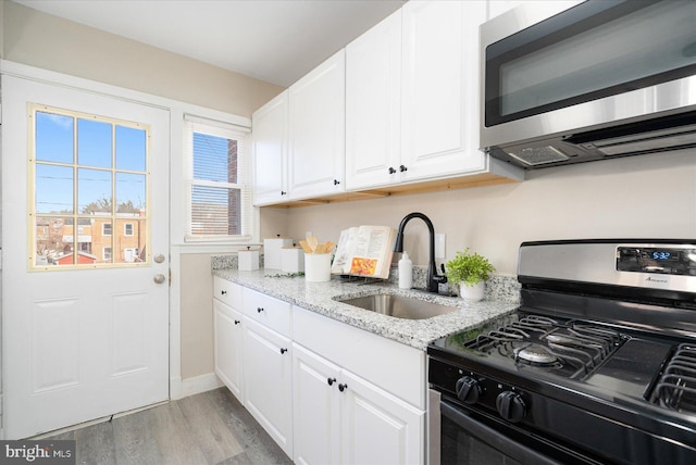 kitchen featuring gas range, light hardwood / wood-style flooring, light stone countertops, sink, and white cabinets